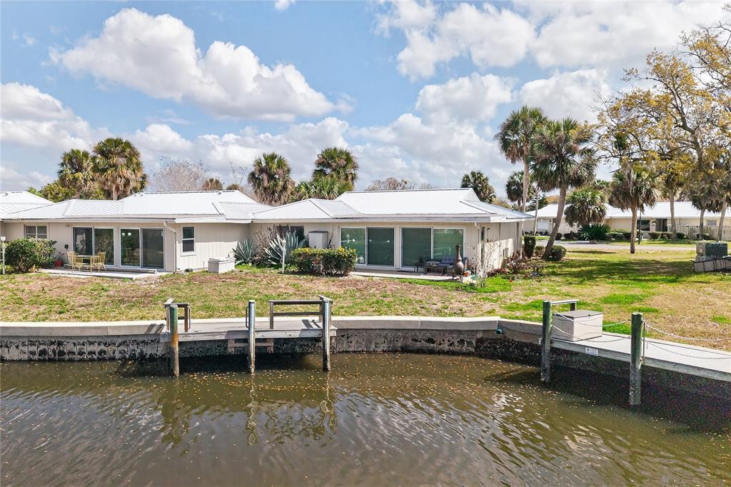 A waterfront view of a single-story house with a wooden dock and palm trees — 11607 W KINGFISHER COURT UNIT 198, CRYSTAL RIVER, FL