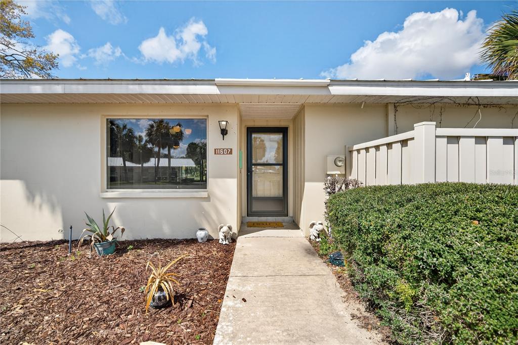The exterior of a single-story home features a concrete walkway leading to a glass storm door — 11607 W KINGFISHER COURT UNIT 198, CRYSTAL RIVER, FL