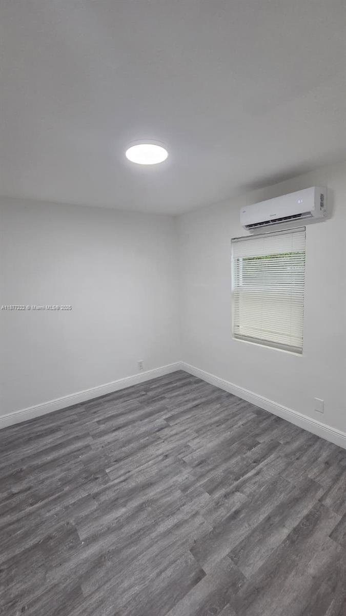 An empty bedroom features gray wood-look flooring, white walls, a ceiling light, and a wall-mounted air conditioner — 855 NW 3rd Ter # 6, Dania Beach FL 33004, DANIA BEACH, FL
