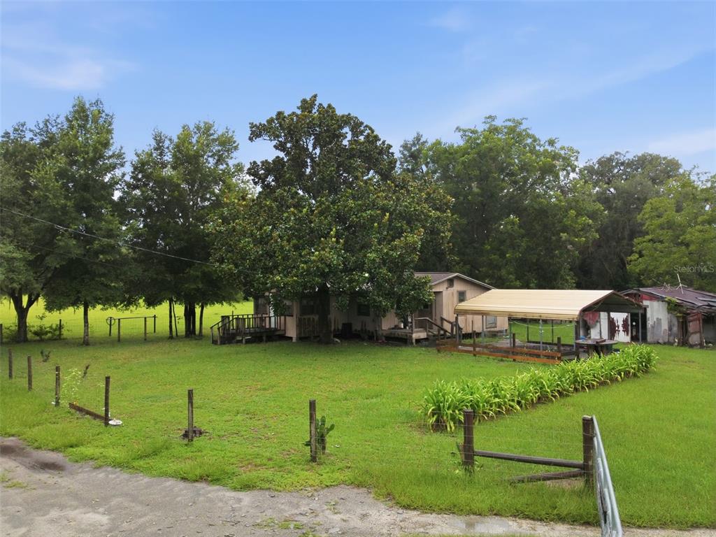 A single-story house with a metal carport sits on a grassy lot with mature trees — 9299 WEATHERLY ROAD, BROOKSVILLE, FL
