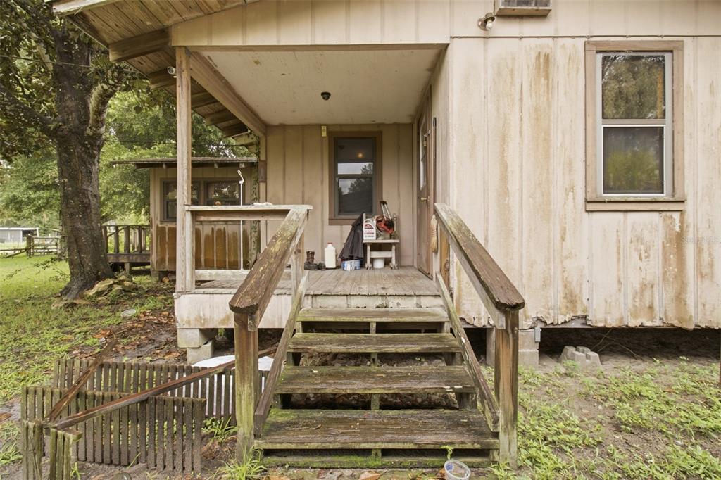 A weathered wooden porch with stairs leads to the entrance of a rustic, light-brown house — 9299 WEATHERLY ROAD, BROOKSVILLE, FL