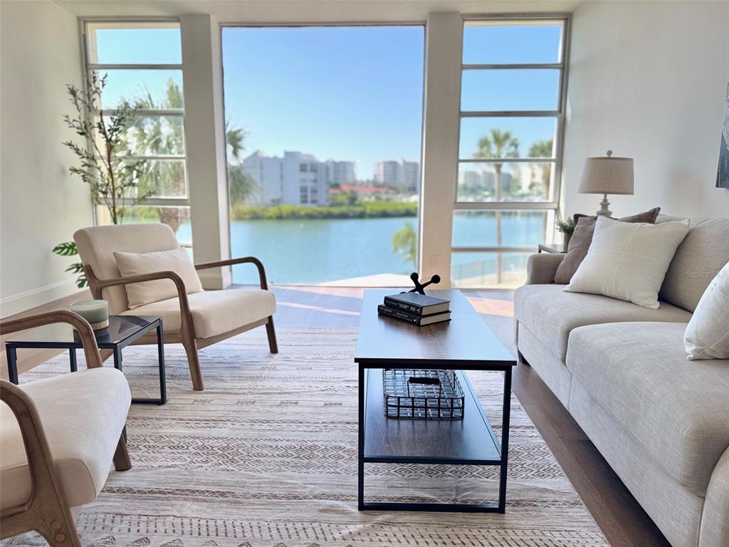 A living room features a sofa, armchairs, and floor-to-ceiling windows overlooking a waterfront view — 7400 SUN ISLAND DRIVE S UNIT 202, SOUTH PASADENA, FL