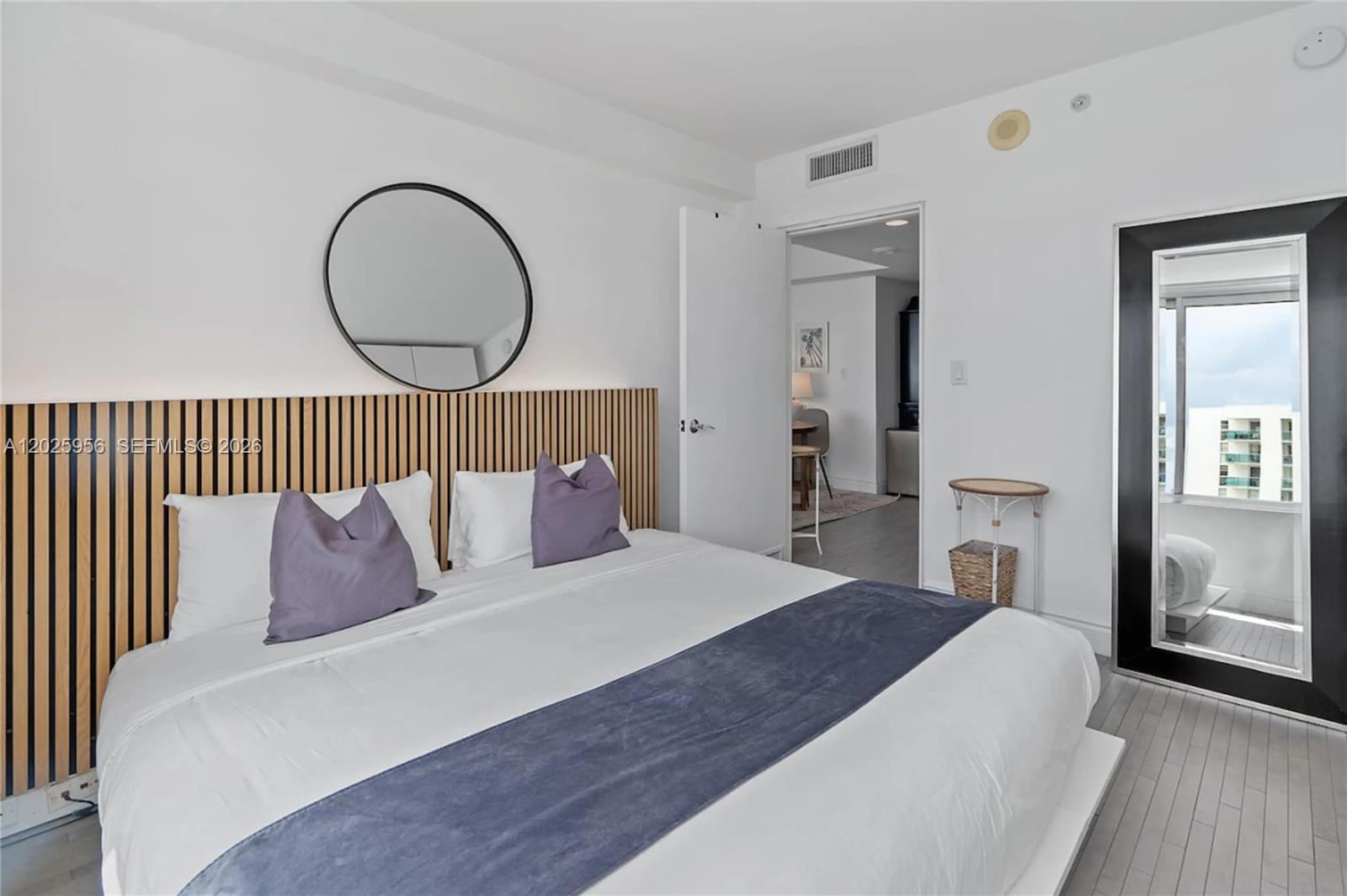 A bedroom features a slatted wood headboard, a round mirror, and a full-length floor mirror — 1100 West Ave # 427, Miami Beach FL 33139, MIAMI BEACH, FL