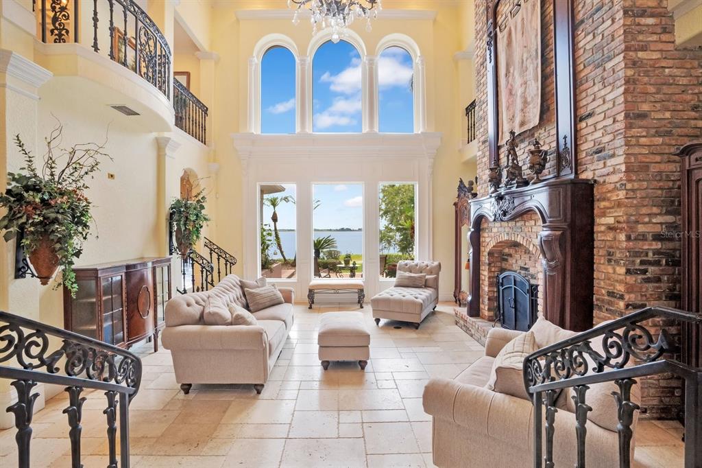 A two-story living room features a stone fireplace, arched windows, and a view of water — 133 VAN FLEET COURT, AUBURNDALE, FL