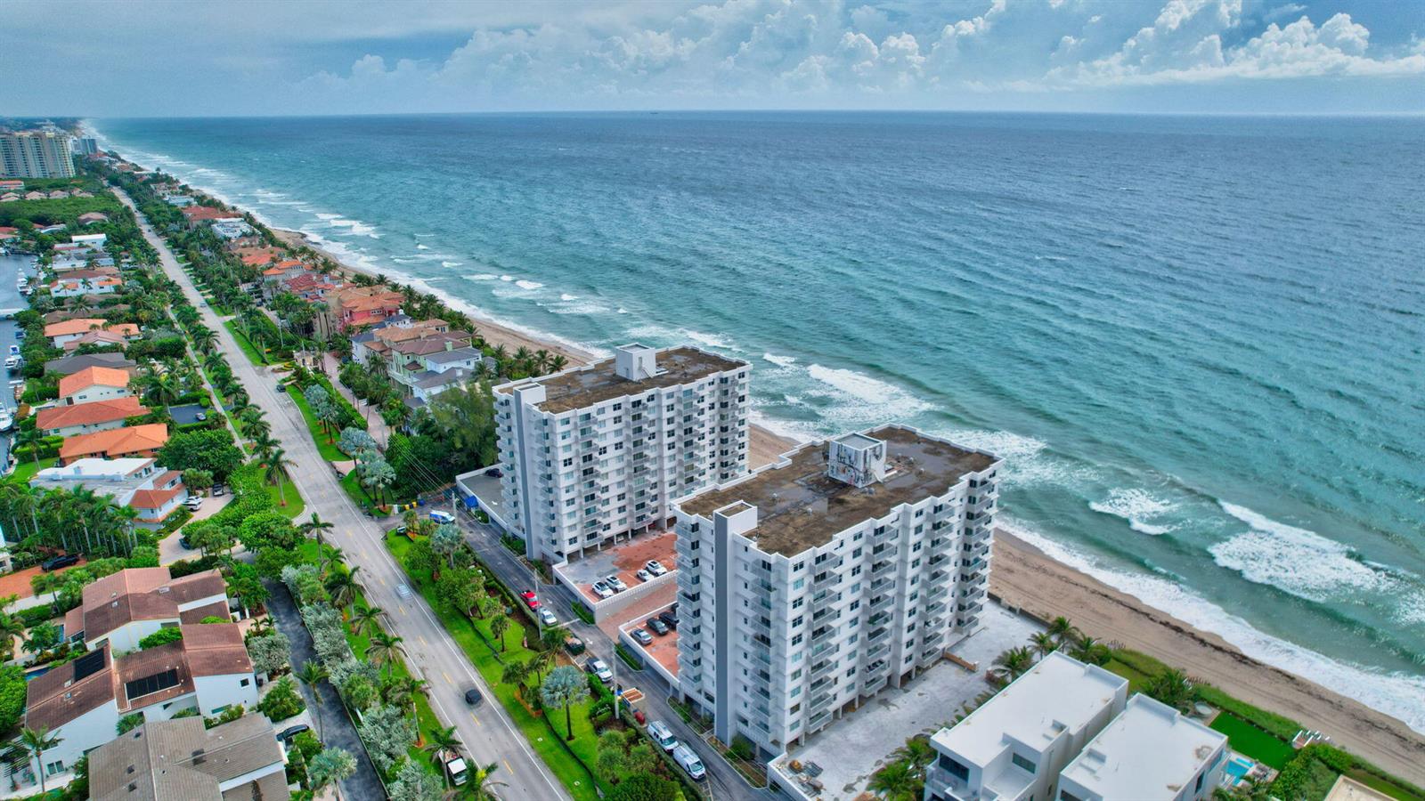 An aerial view shows two white apartment buildings situated between a coastal road and the ocean — 4511 S Ocean Boulevard # 401, Highland Beach FL 33487, HIGHLAND BEACH, FL
