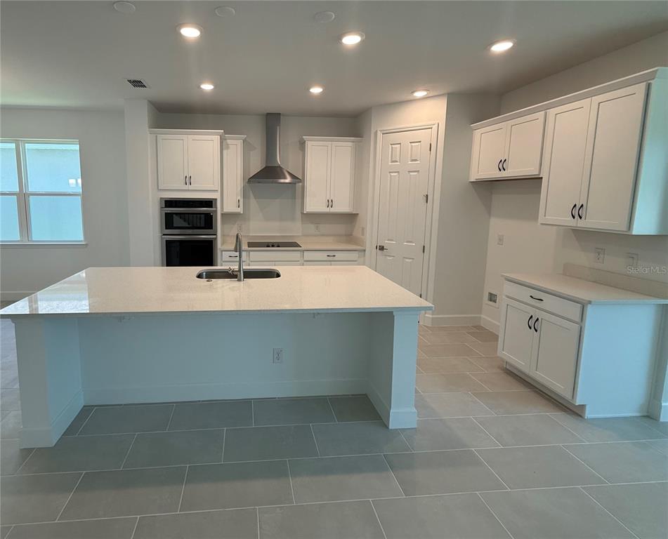 A modern kitchen features white cabinets, a large quartz island, and light gray tile flooring — 2680 CAVANAUGH DRIVE, ORLANDO, FL