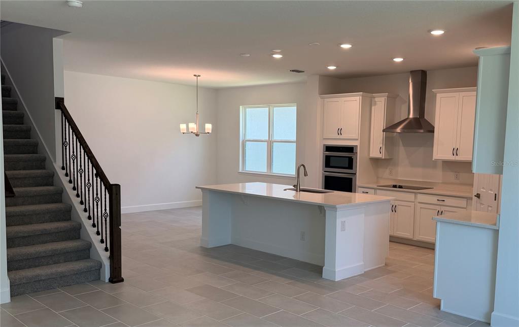 A modern kitchen features white cabinetry, a central island, and an adjacent staircase with railing — 2680 CAVANAUGH DRIVE, ORLANDO, FL