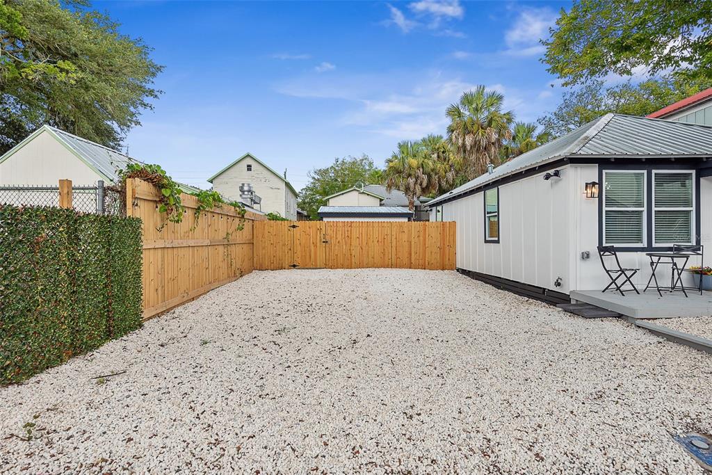 A gravel backyard features a wooden fence, a gate, and a white house exterior — 63 ONEIDA STREET, ST AUGUSTINE, FL