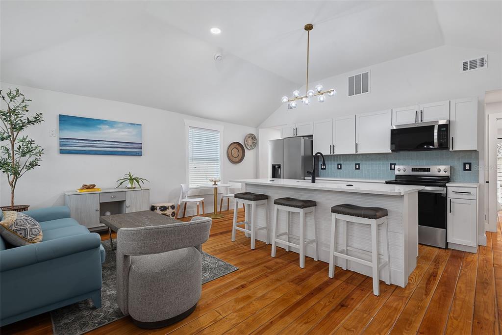 An open-concept kitchen and living area features white cabinetry, a breakfast bar, and wood flooring — 63 ONEIDA STREET, ST AUGUSTINE, FL
