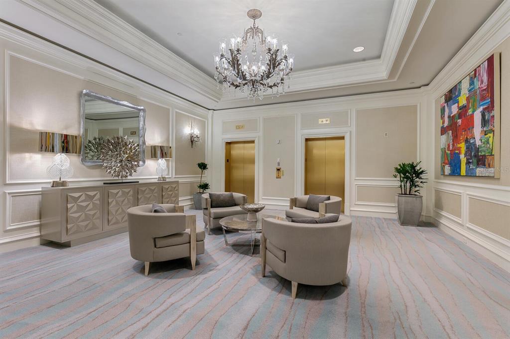 A formal lobby features a crystal chandelier, two gold elevators, four armchairs, and patterned carpeting — 1111 RITZ CARLTON DRIVE UNIT 1803, SARASOTA, FL