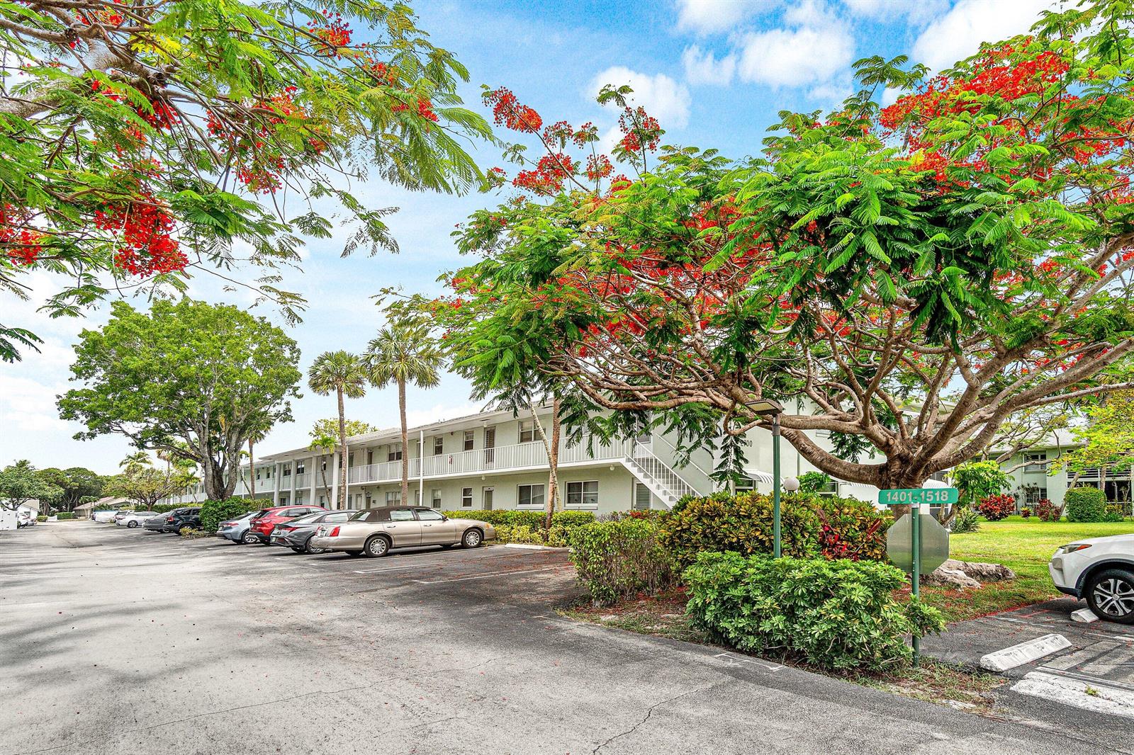 A multi-story apartment building with a parking lot and blooming trees in the foreground — 2700 SW 22nd Avenue # 1409, Delray Beach FL 33445, DELRAY BEACH, FL
