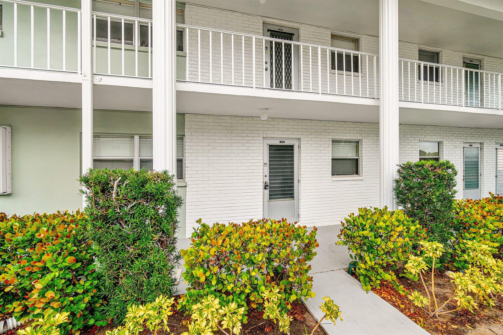 A two-story apartment building features white brick walls, white railings, and a landscaped walkway — 2700 SW 22nd Avenue # 1409, Delray Beach FL 33445, DELRAY BEACH, FL