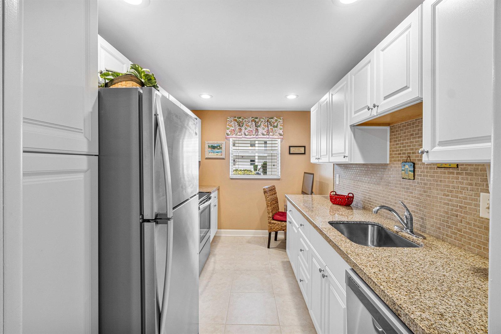 A galley kitchen features white cabinets, granite countertops, a stainless steel refrigerator, and tile flooring — 2700 SW 22nd Avenue # 1409, Delray Beach FL 33445, DELRAY BEACH, FL