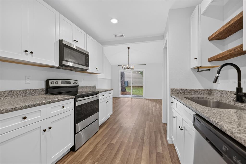 A kitchen with white cabinets, granite countertops, stainless steel appliances, and wood-look flooring — 16640 SE 59TH PLACE, OCKLAWAHA, FL