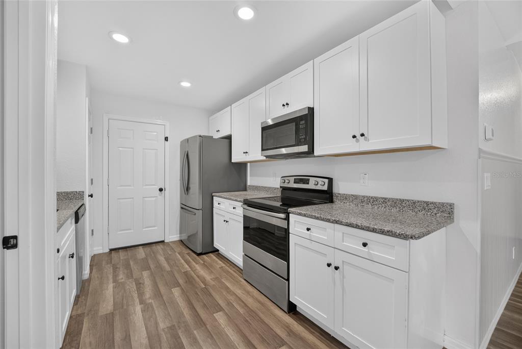 A kitchen with white cabinets, stainless steel appliances, granite countertops, and wood-look flooring — 16640 SE 59TH PLACE, OCKLAWAHA, FL