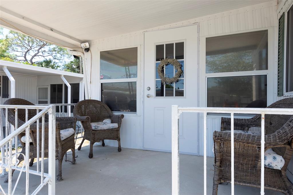 A covered porch features three wicker chairs, a white front door, and metal railings — 4368 72ND WAY N UNIT 111, ST PETERSBURG, FL