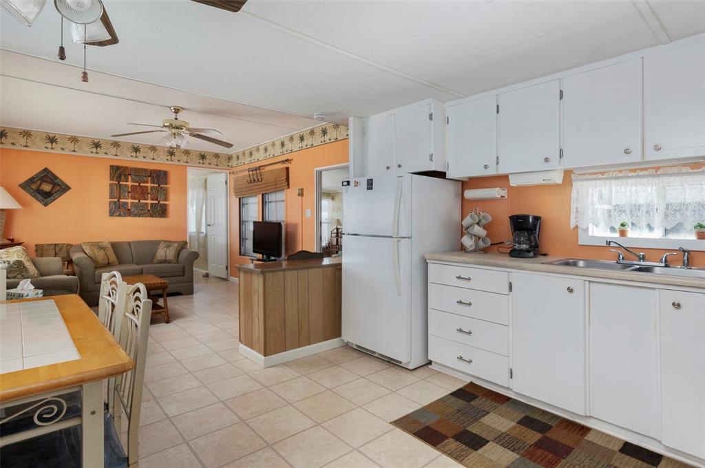 A kitchen with white cabinets and appliances opens into a living room with orange walls — 4368 72ND WAY N UNIT 111, ST PETERSBURG, FL