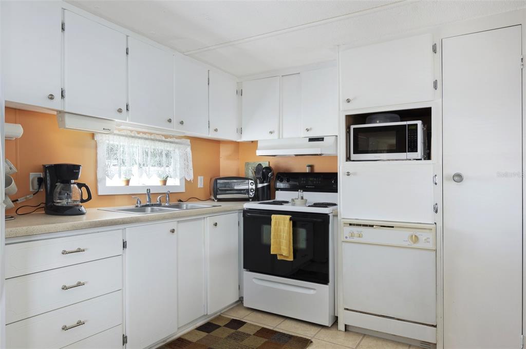 A kitchen with white cabinets, orange walls, a black stove, and a built-in microwave — 4368 72ND WAY N UNIT 111, ST PETERSBURG, FL