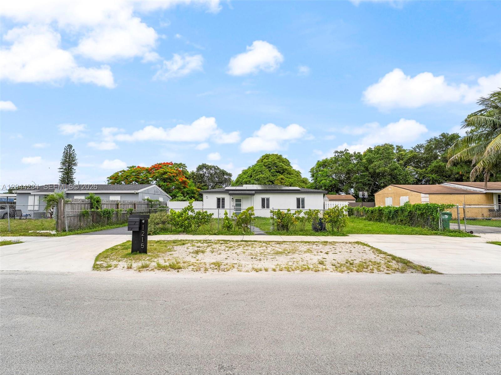 A single-story white house with solar panels sits behind a chain-link fence and driveway — 1215 Kasim ST, Opa-Locka FL 33054, OPA-LOCKA, FL