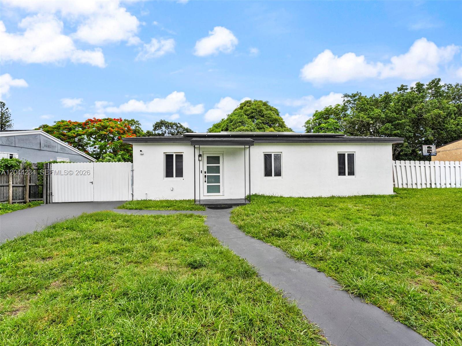 A white, single-story house features a central front door, three windows, and a paved walkway — 1215 Kasim ST, Opa-Locka FL 33054, OPA-LOCKA, FL