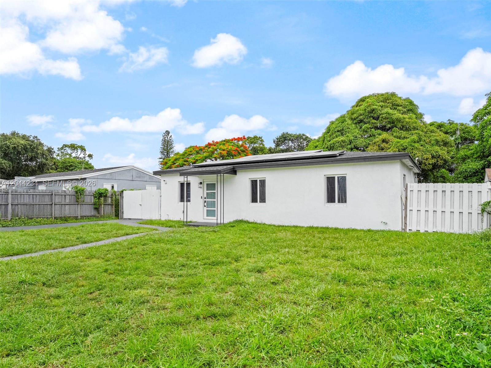 A white single-story house with a flat roof and solar panels sits on a lawn — 1215 Kasim ST, Opa-Locka FL 33054, OPA-LOCKA, FL