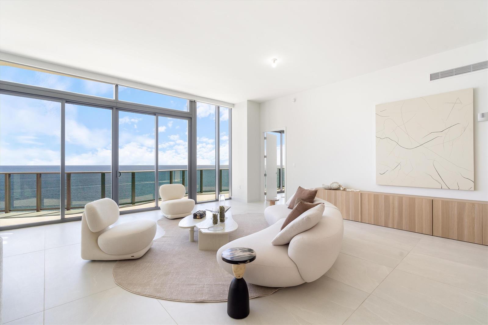 A modern living room features a curved sofa, white chairs, and floor-to-ceiling ocean views — 900 N Ocean Boulevard, Pompano Beach FL 33062, POMPANO BEACH, FL