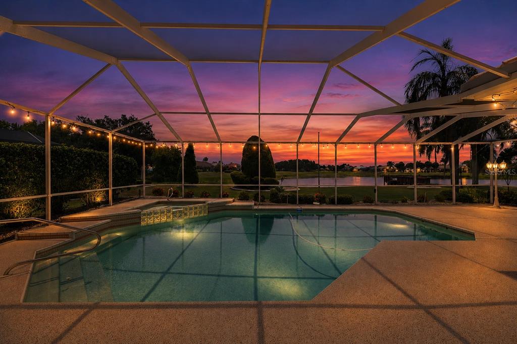 A screened-in swimming pool and spa overlook a lake at sunset — 2116 PLATINUM DRIVE, SUN CITY CENTER, FL