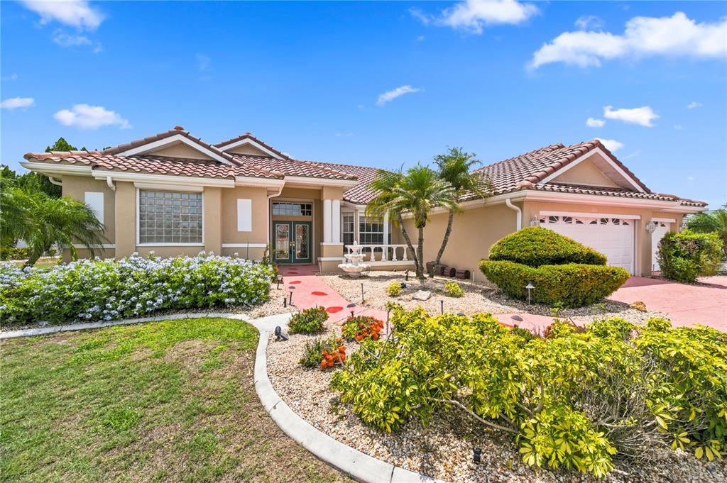 A single-story house with a tiled roof, tan stucco exterior, and a landscaped front yard — 2116 PLATINUM DRIVE, SUN CITY CENTER, FL