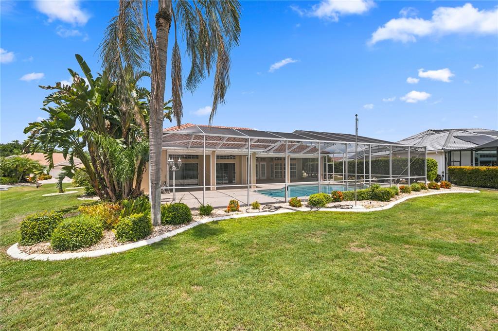 A backyard features a screened-in swimming pool, a palm tree, and landscaped garden beds — 2116 PLATINUM DRIVE, SUN CITY CENTER, FL