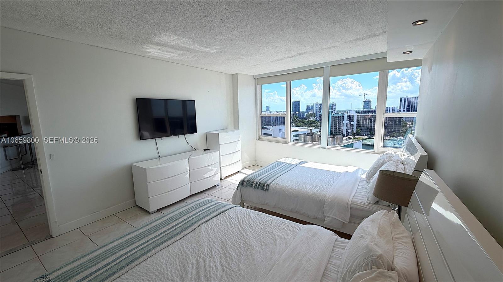 A bedroom with two beds, white furniture, and large windows overlooking a city skyline — 3505 S Ocean Dr # 1403, Hollywood FL 33019, HOLLYWOOD, FL
