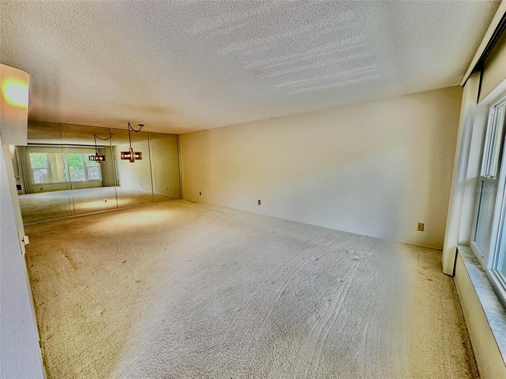 An empty room features beige wall-to-wall carpeting, a large mirrored wall, and a side window — 2220 SPANISH DRIVE UNIT 26, CLEARWATER, FL