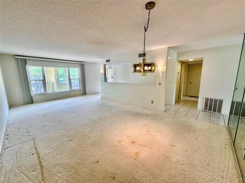 A spacious living room features beige wall-to-wall carpeting, a large window, and a hanging chandelier — 2220 SPANISH DRIVE UNIT 26, CLEARWATER, FL