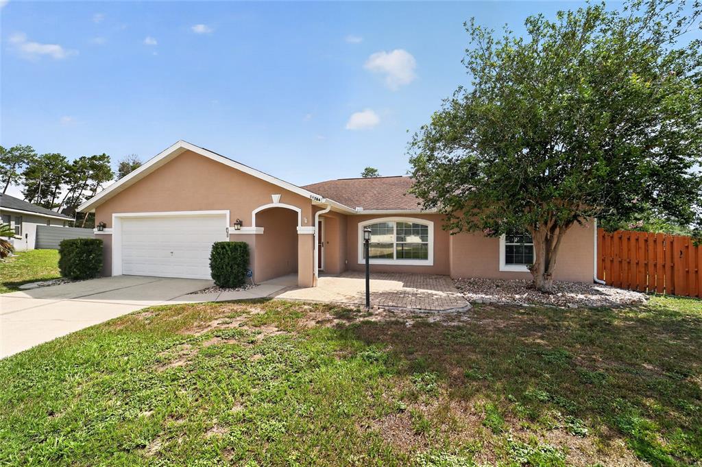 A single-story house with a tan stucco exterior, a two-car garage, and a paved entryway — 10384 SW 41ST COURT, OCALA, FL