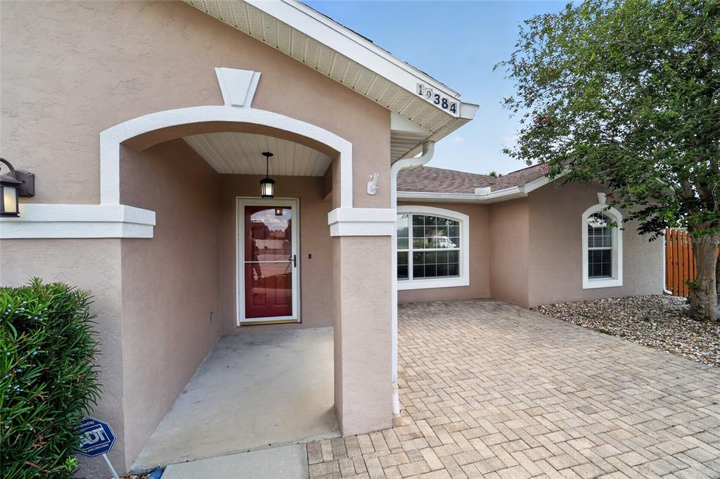 The exterior of a beige house features a covered entryway, a brick-paved patio, and windows — 10384 SW 41ST COURT, OCALA, FL