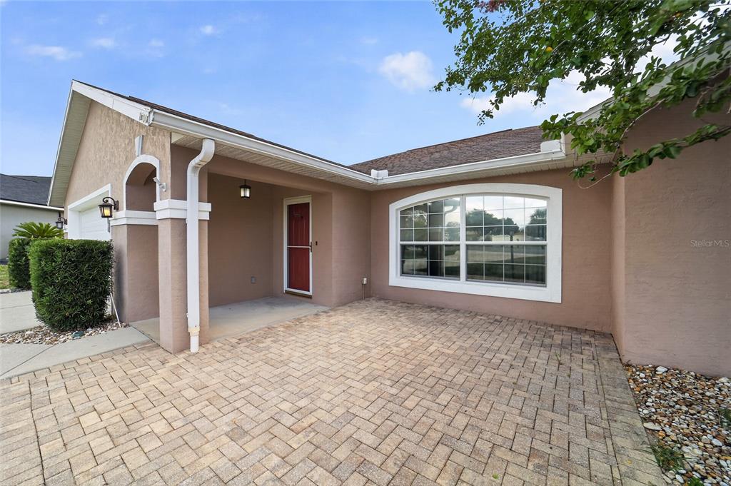 A paved front patio leads to the entrance of a house with tan stucco walls — 10384 SW 41ST COURT, OCALA, FL