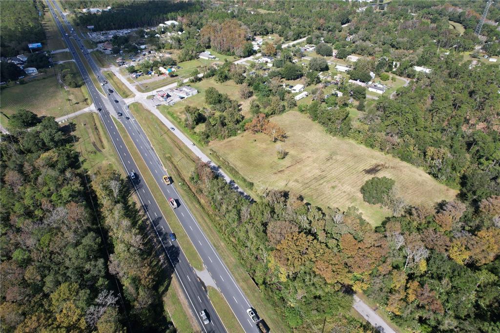 An aerial view shows a large, grassy vacant lot adjacent to a multi-lane highway — 18049 OLD CHENEY HWY, ORLANDO, FL