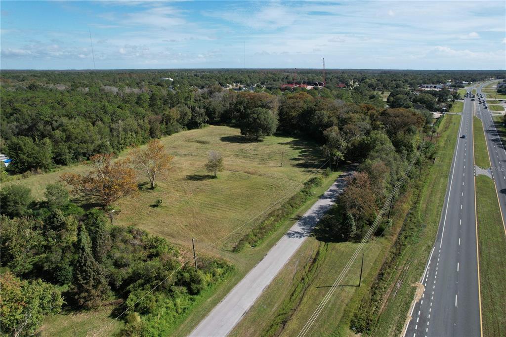 An aerial view shows a large, grassy vacant lot adjacent to a paved highway — 18049 OLD CHENEY HWY, ORLANDO, FL