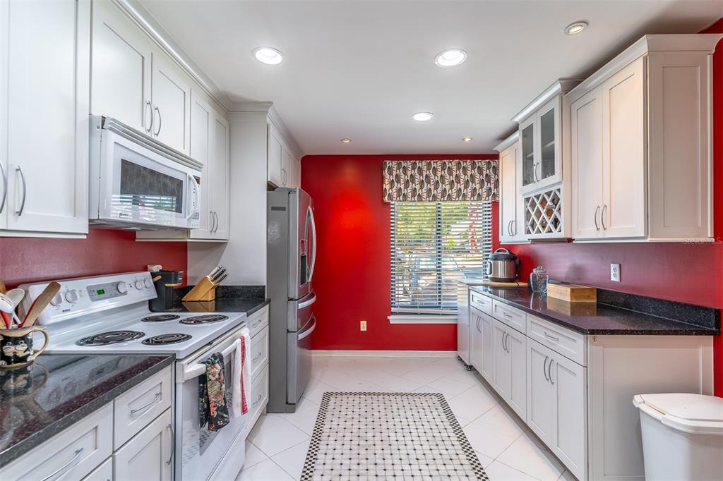 A kitchen features white cabinetry, black countertops, stainless steel appliances, and a bold red wall — 2503 TAHOE CIRCLE UNIT 2503, WINTER PARK, FL