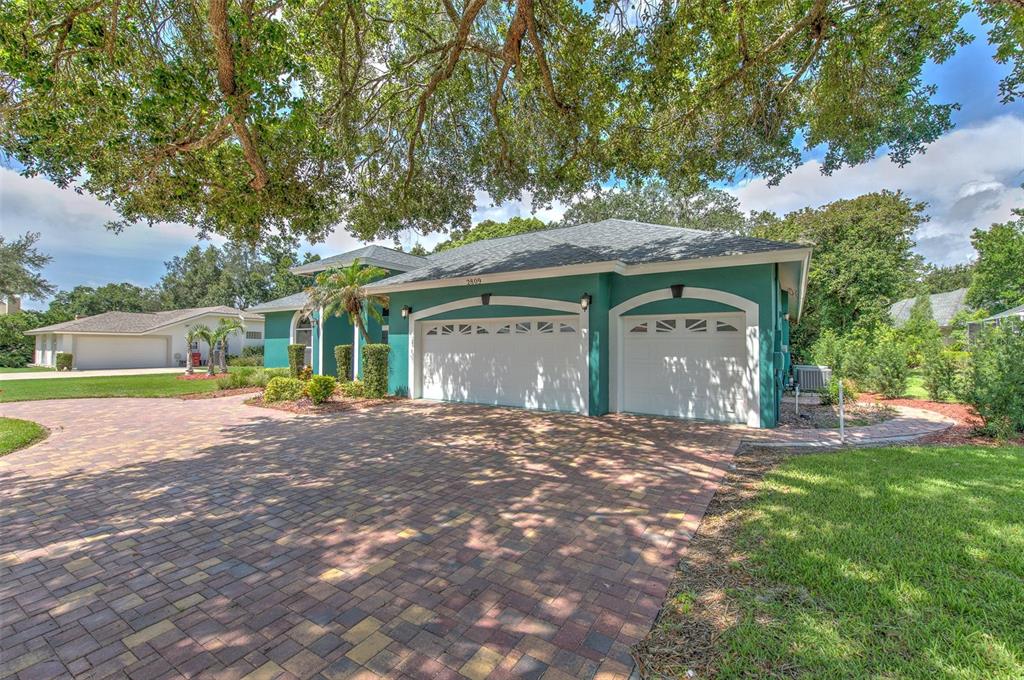 A teal house with a three-car garage and a large paver driveway under oak trees — 2809 BARRET AVENUE, PLANT CITY, FL