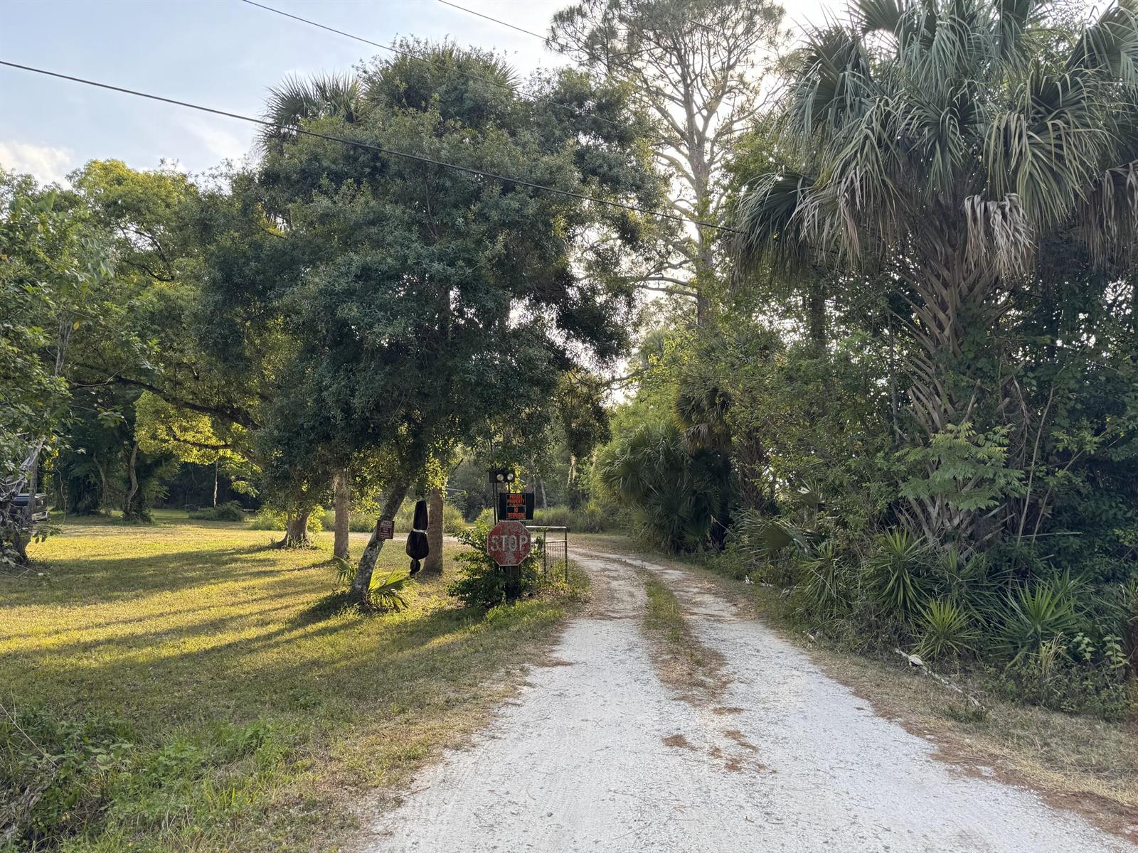 A gravel driveway leads toward a stop sign and a gated entrance surrounded by trees — 2289 NW 32nd Drive, Okeechobee FL 34972, OKEECHOBEE, FL