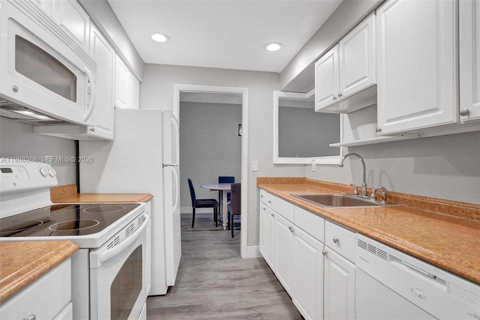 A white kitchen features orange laminate countertops, stainless steel appliances, and gray wood-look flooring — 400 N Riverside Dr # 214, Pompano Beach FL 33062, POMPANO BEACH, FL