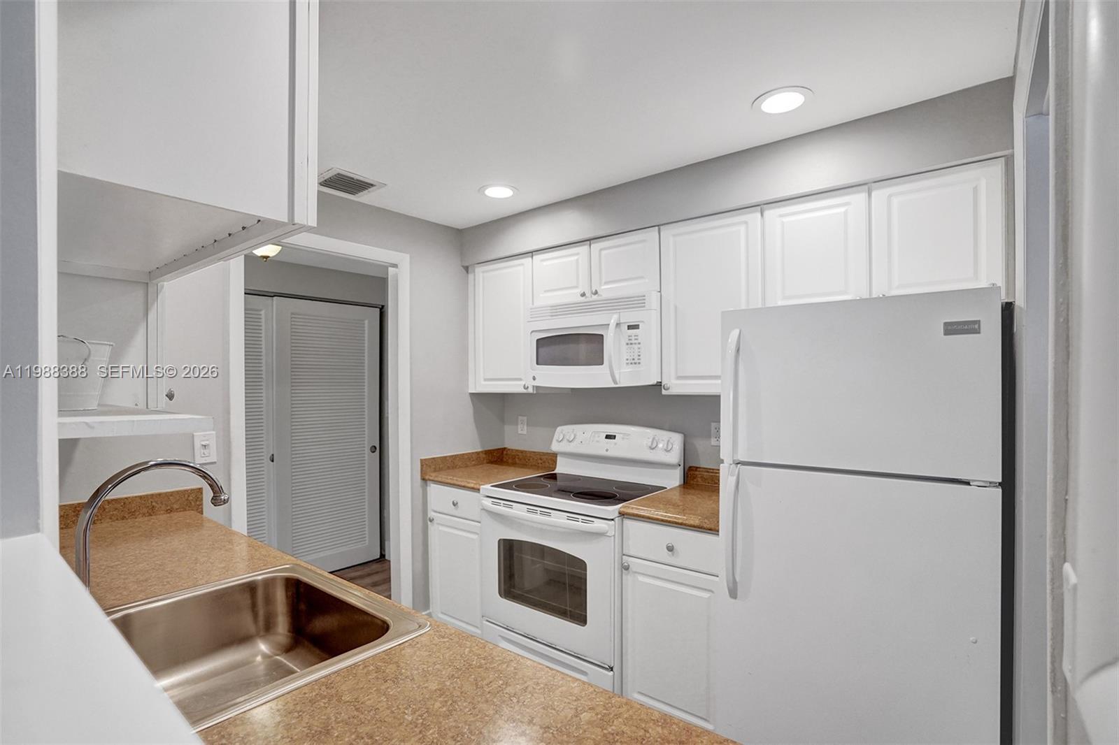 A kitchen features white cabinets, a white stove, a microwave, and a stainless steel sink — 400 N Riverside Dr # 214, Pompano Beach FL 33062, POMPANO BEACH, FL