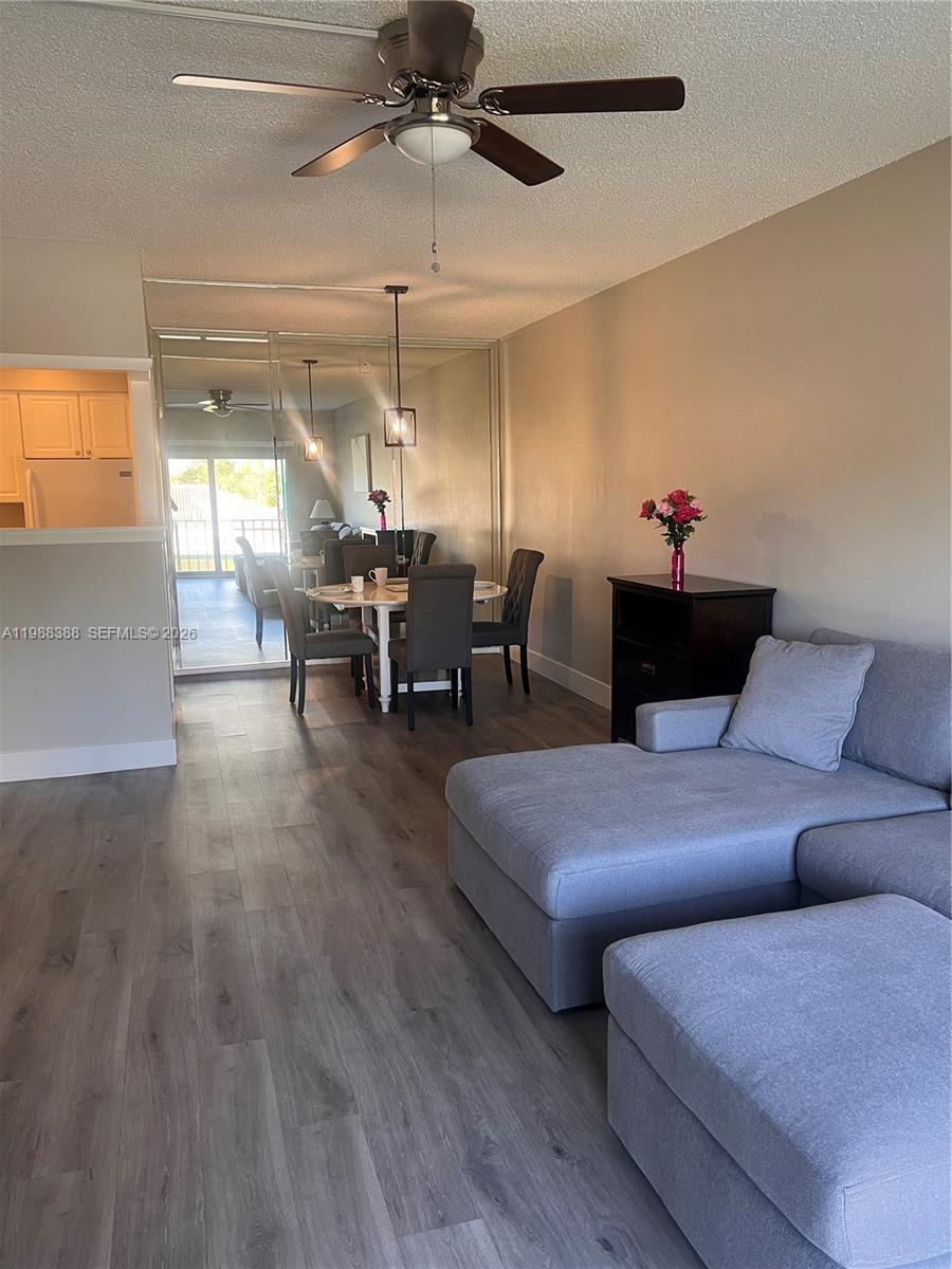 A living room with gray flooring features a sectional sofa, dining area, and mirrored wall — 400 N Riverside Dr # 214, Pompano Beach FL 33062, POMPANO BEACH, FL