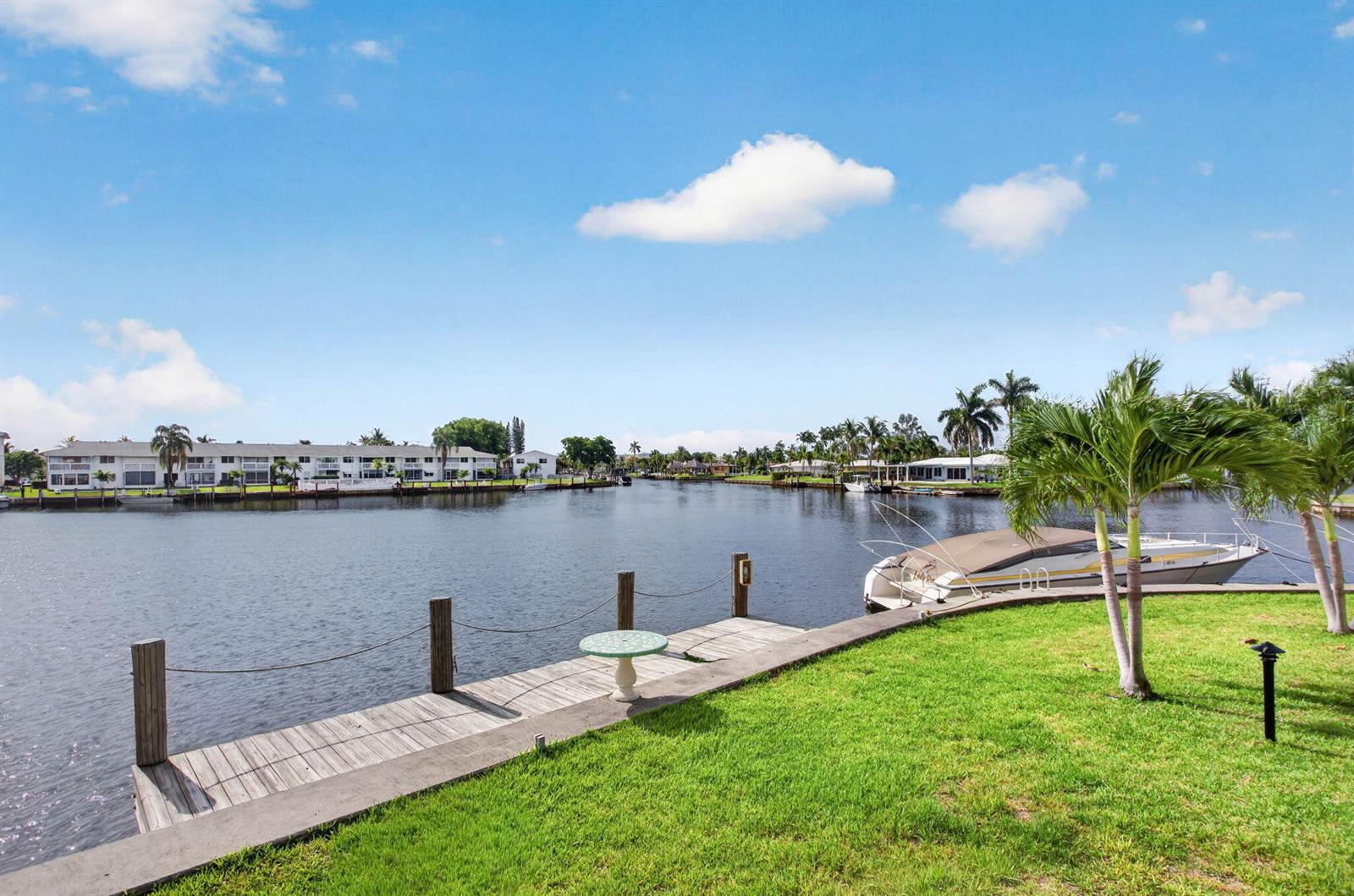 A wooden dock extends into a canal with a boat moored nearby on a sunny day — 298 SE 6th Avenue # 9, Pompano Beach FL 33060, POMPANO BEACH, FL