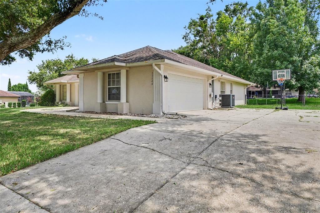 A beige single-story house features a two-car garage, a concrete driveway, and a basketball hoop — 11648 GRAND BAY BOULEVARD, CLERMONT, FL