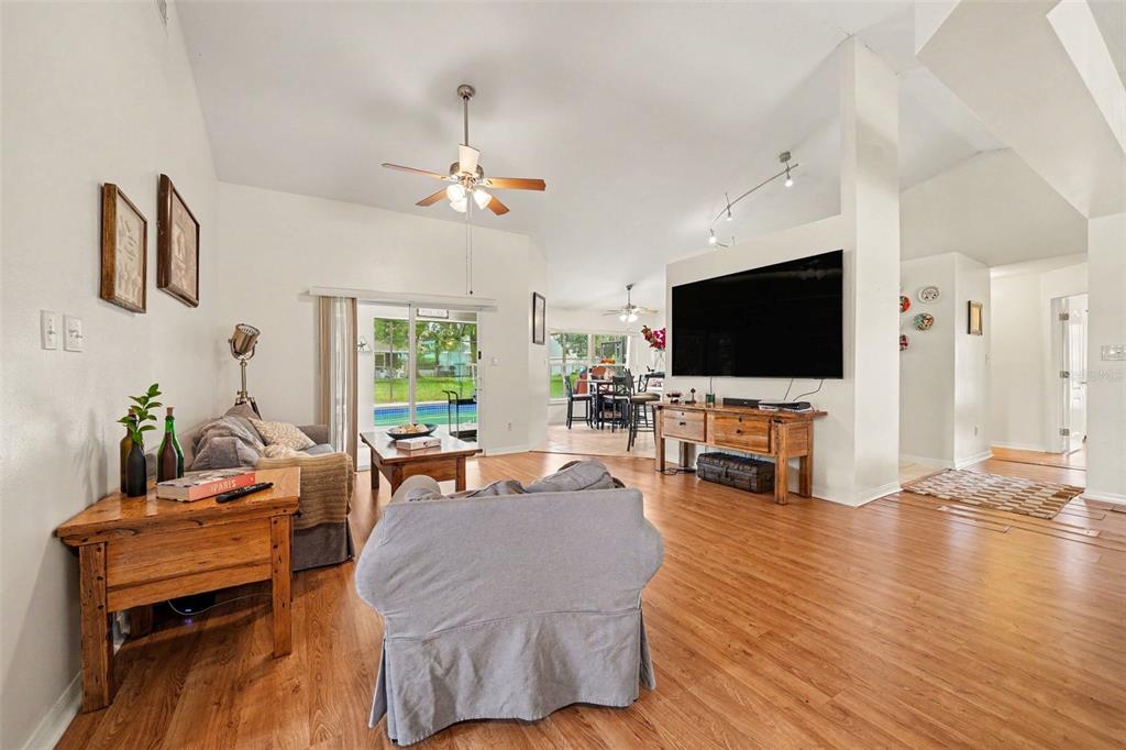 A living room with wood-look flooring, a large wall-mounted television, and a sliding glass door — 11648 GRAND BAY BOULEVARD, CLERMONT, FL