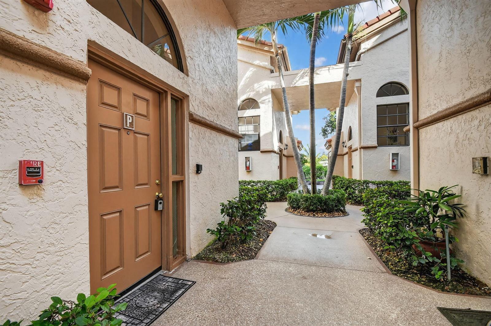 An exterior view of a building entrance with a brown door and a palm tree courtyard — 5187 Europa Drive # P, Boynton Beach FL 33437, BOYNTON BEACH, FL