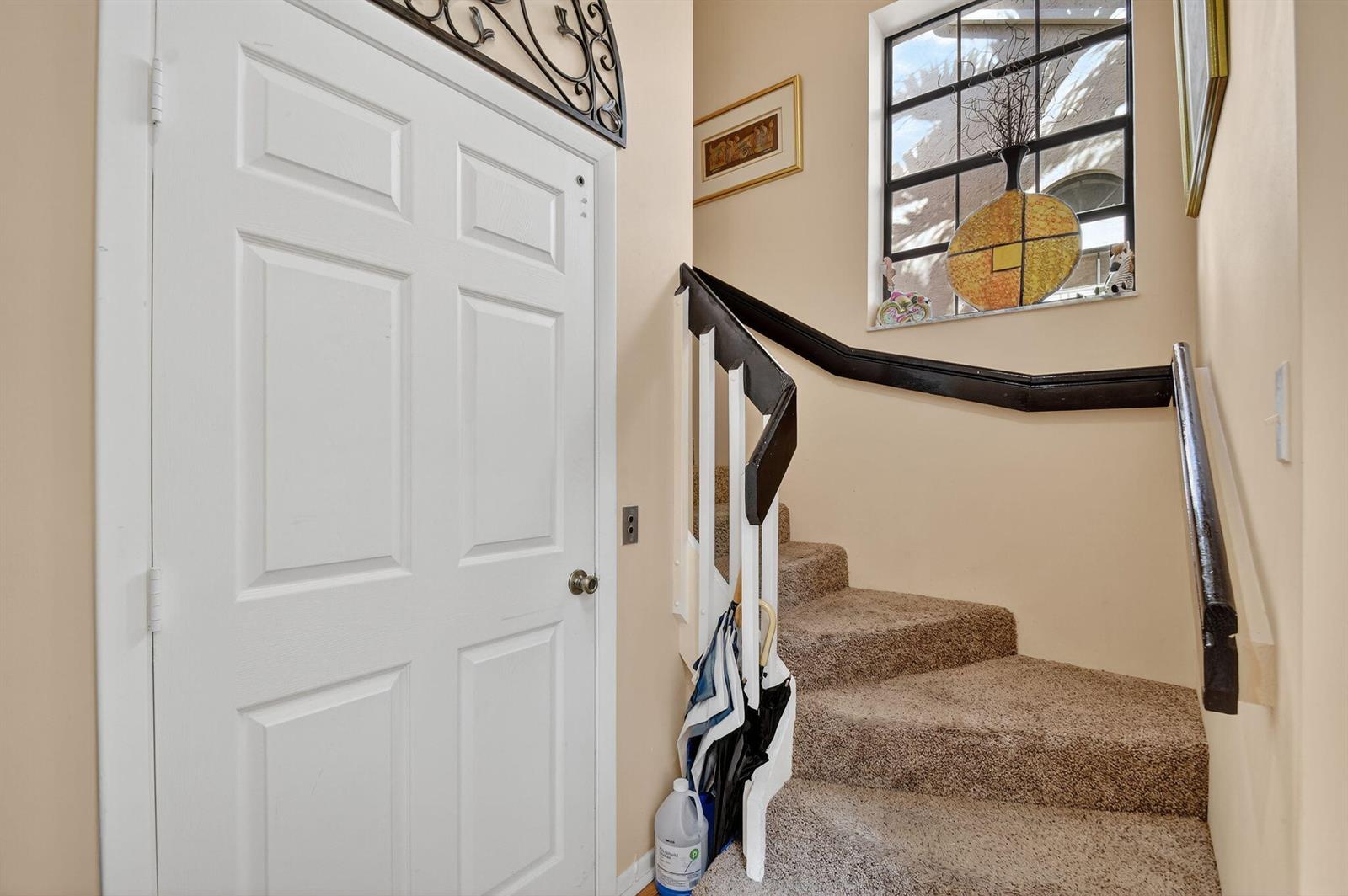A white door stands next to a carpeted staircase with a black handrail and window — 5187 Europa Drive # P, Boynton Beach FL 33437, BOYNTON BEACH, FL