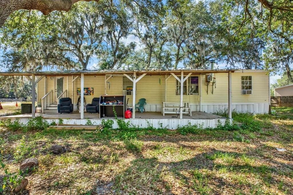 A single-story mobile home with a covered front porch sits under large, moss-draped oak trees — 3642 KALMAN DRIVE, ZEPHYRHILLS, FL