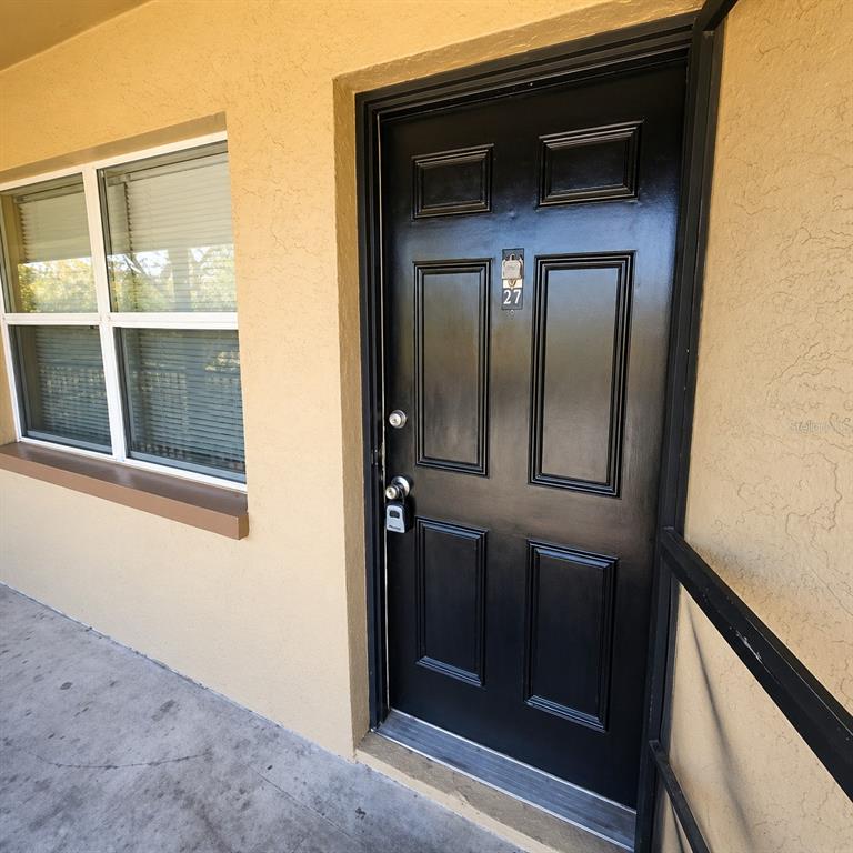 A black front door with a lockbox and a window are on a tan exterior wall — 2501 HARN BOULEVARD UNIT H27, CLEARWATER, FL